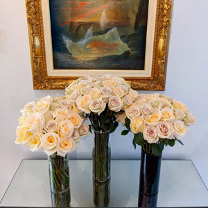 3 vases on table of Cream color roses with hints of purple and orange. 