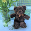 Dark brown teddy bear next to a vase and candle