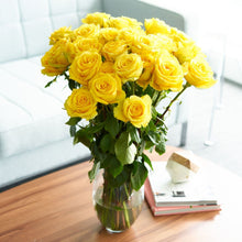 Bouquet in glass vase of bright yellow long stem roses with golden sun like quality 

